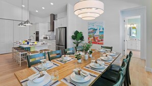 Una cocina moderna con armarios blancos, electrodomésticos de acero inoxidable y un comedor con una mesa de madera para seis comensales.