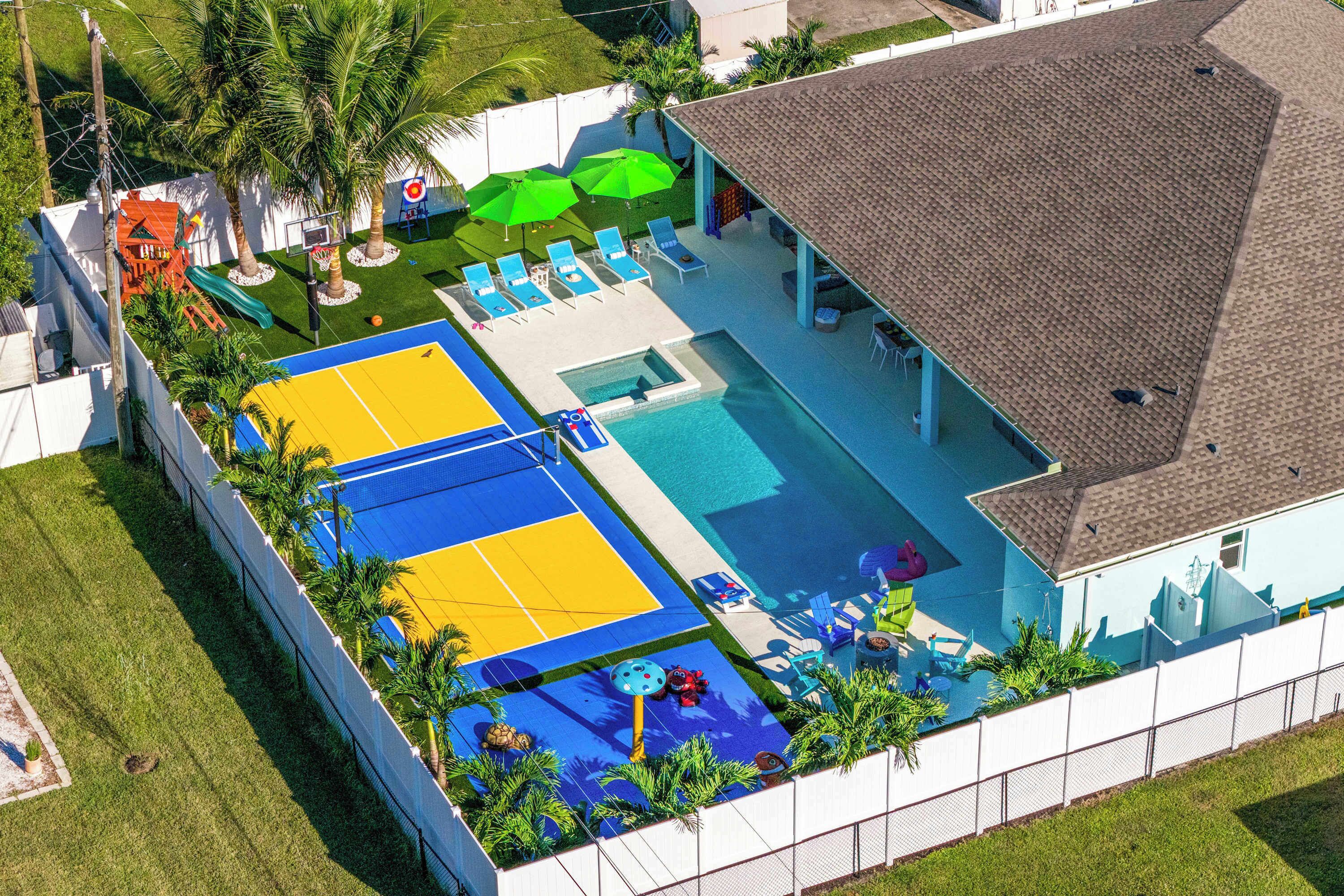 A residential property with a swimming pool, a basketball court, and a patio area with lounge chairs and umbrellas.