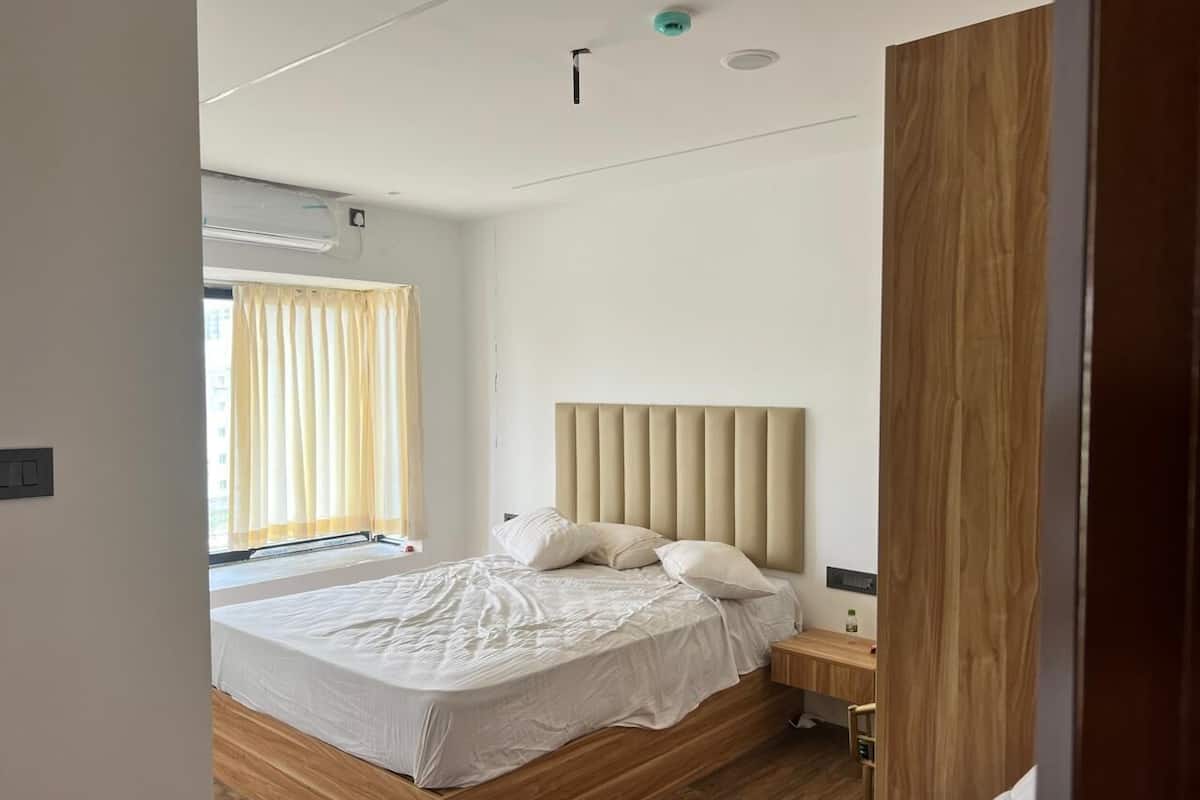 Egy modern hálószoba, amelyben egy nagy ágy, egy fafejű ágykeret, egy éjjeliszemély és egy függönnyel ellátott ablak található.