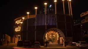 Ein Gebäude mit einem markanten Eingang, beleuchtet von mehreren Lichtern, und einer Schilderung, die es als Hotel kennzeichnet.
