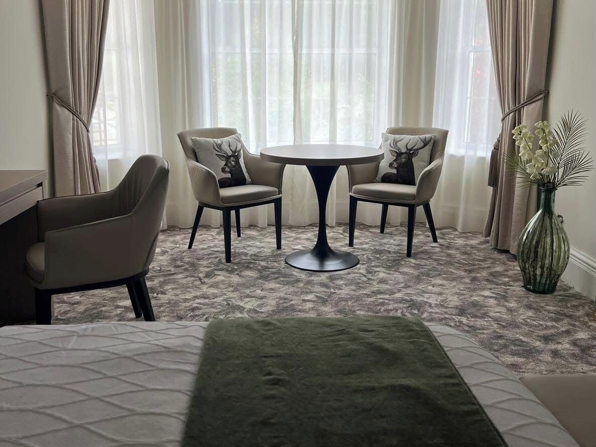 Ein Hotelzimmer mit einem Bett, zwei Stühlen, einem kleinen runden Tisch und einer Vase mit Blumen.