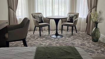 Una habitación de hotel con una cama, dos sillas, una mesita redonda y un florero con flores.