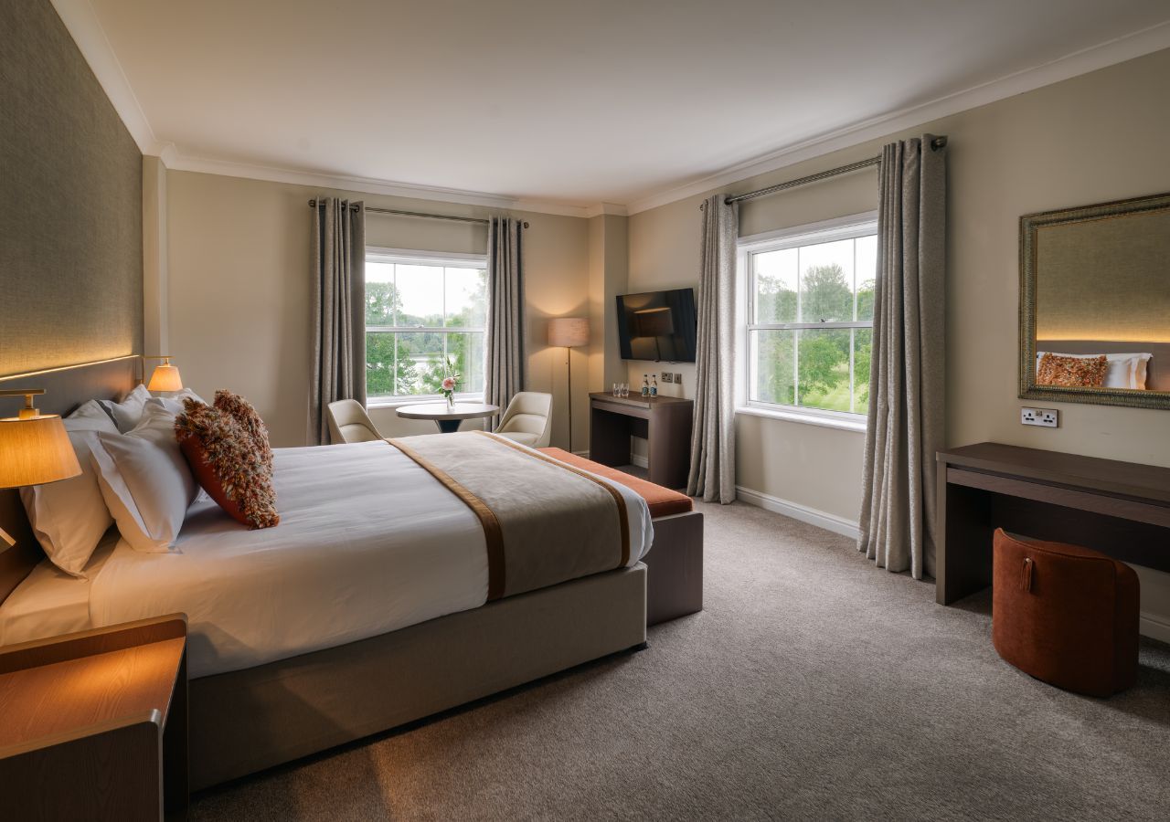 Habitación de hotel con una cama grande, un escritorio, una silla, un televisor y vistas al exterior.
