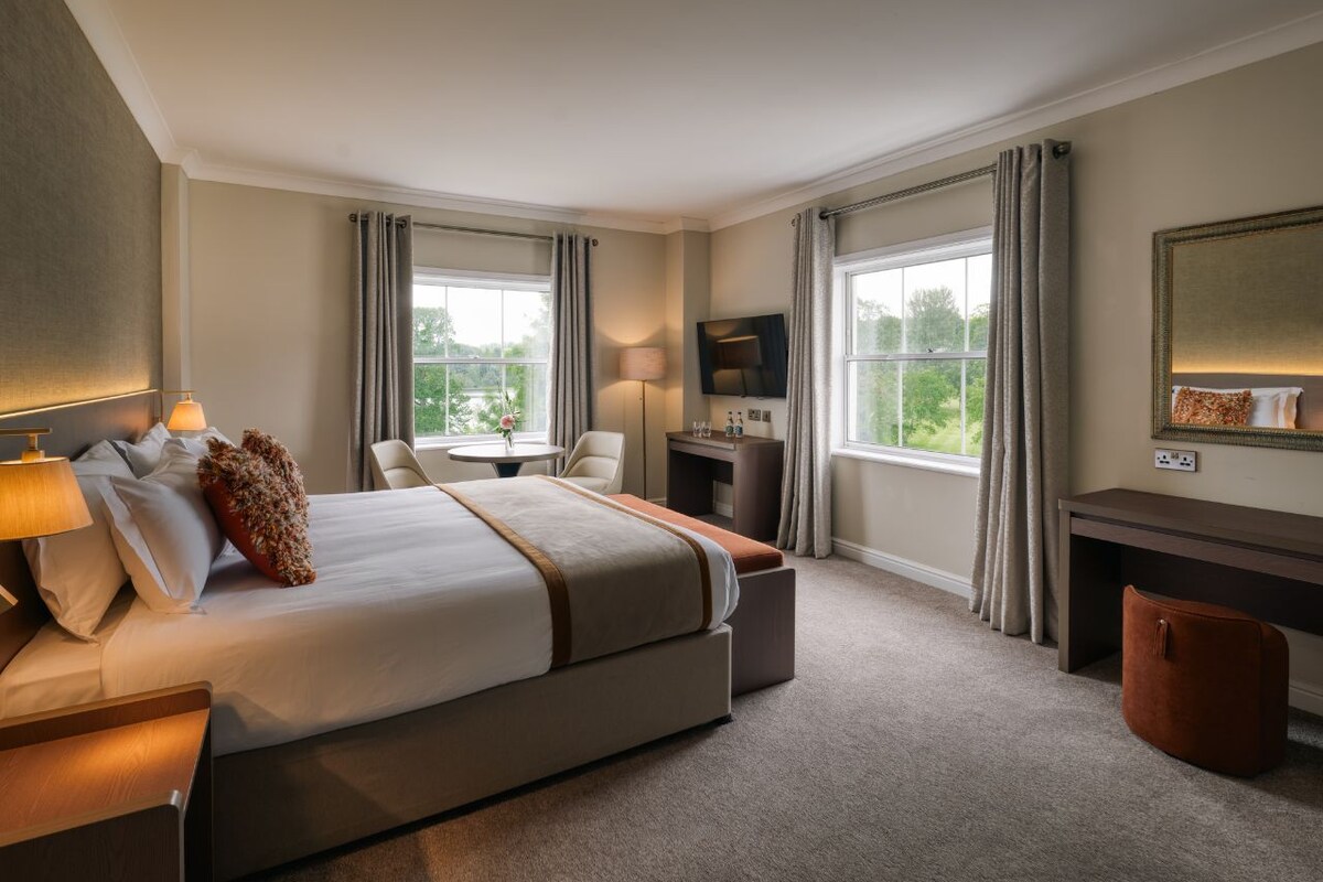 Habitación de hotel con una cama grande, un escritorio, una silla, un televisor y vistas al exterior.