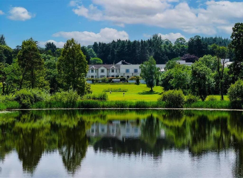 A lakeside property with a large house, manicured lawn, and a reflection in the water.