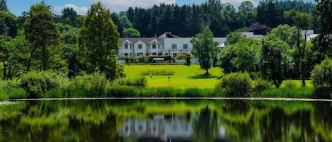 Una propiedad frente al lago con una casa grande, césped cuidado y un reflejo en el agua.