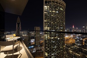 A high-rise building with a unique facade, a dining area with a table and chairs, and a cityscape view at night.