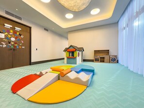 A play area with soft play mats, a small playhouse, and a laundry station.