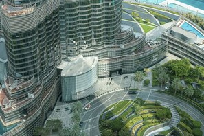 A modern high-rise building with a curved glass facade, a landscaped area with palm trees, and a roundabout with vehicles.