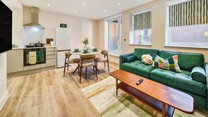 Een moderne woonkamer met een groene bank, een houten salontafel en een eethoek met een ronde tafel en stoelen.
