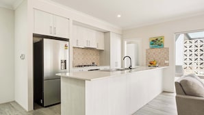 A modern kitchen with white cabinetry, a central island, and a built-in stove. - Quenda Villa (Canning Vale)
