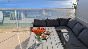 Ein Balkon mit Meerblick, ein Glastisch mit Blumenvase und eine Sitzecke.