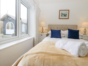 Un dormitorio con una cama grande, dos mesitas de noche con lámparas, una ventana con cortinas y un cuadro enmarcado en la pared.