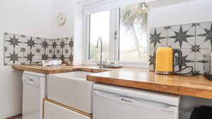 A compact kitchen with a dishwasher, a sink, a window, and a kettle on the countertop.