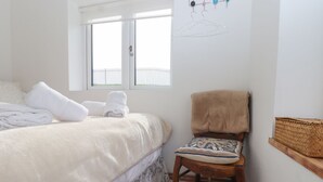 A bedroom with a bed, a chair, a window, and a wall-mounted rack.