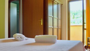 Habitación de hotel con una cama, una toalla doblada, un armario y un ventanal corredero que da a un espacio exterior.
