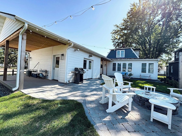 A covered patio area with outdoor seating, a grill, and a small house in the background.