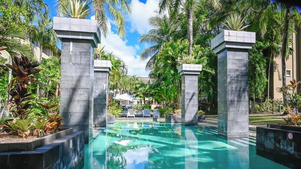 Una piscina con agua cristalina, rodeada de palmeras y un edificio al fondo.