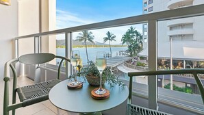 A balcony with a table and chairs, overlooking a body of water and palm trees. - Waterfront Bliss Harbour Lights Gym and City View (Cairns City)