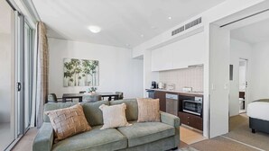 A modern living room with a sofa, a coffee table, and a dining area with a table and chairs. There is a kitchen area with appliances and cabinets. - Waterfront Bliss Harbour Lights Gym and City View (Cairns City)
