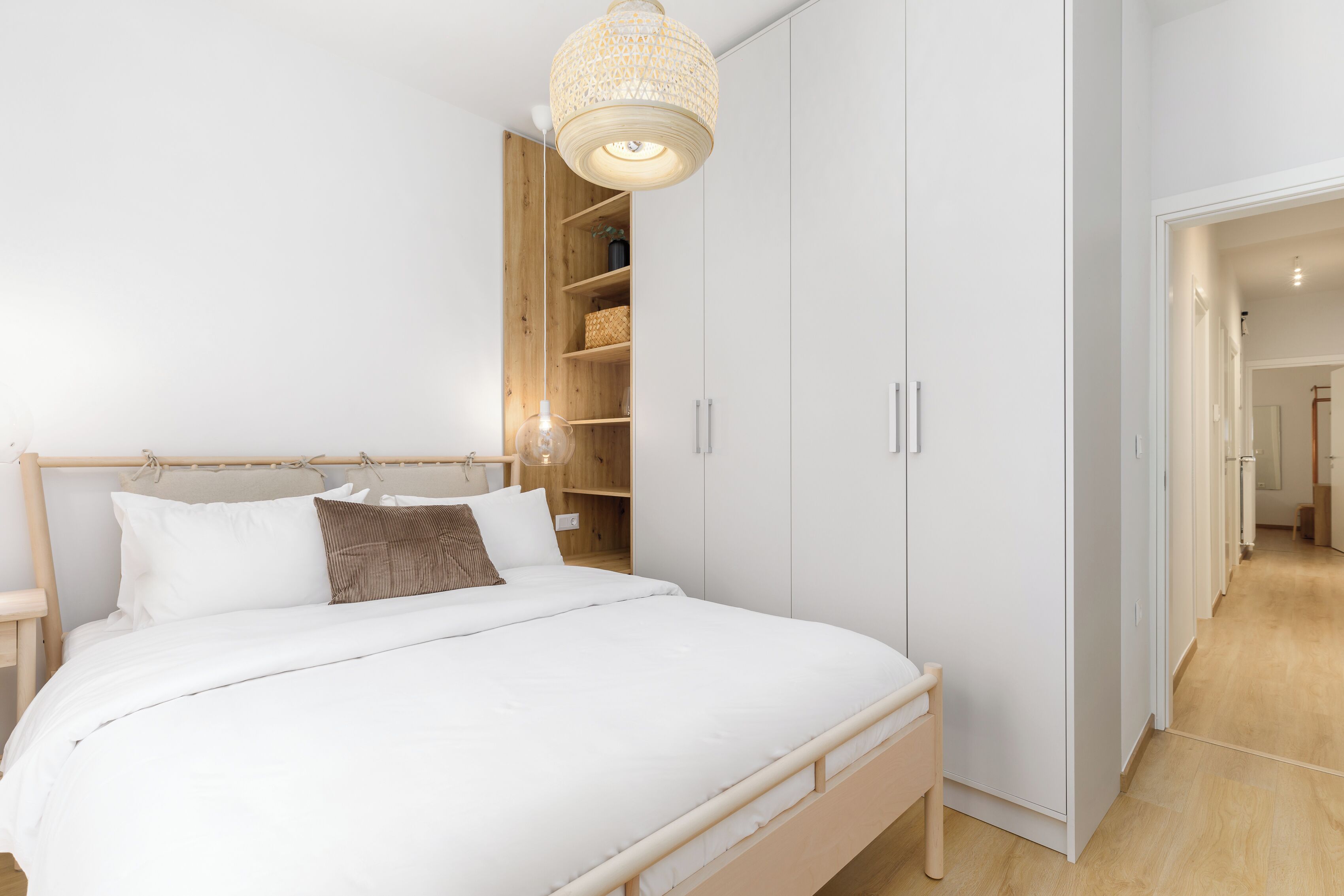 A bedroom with a wooden bed, white bedding, a built-in wardrobe, and a hanging light fixture.