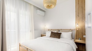 A modern bedroom with a wooden bed, white bedding, a wooden nightstand, and a hanging light fixture. - Bel Air by halu (Thessaloniki)