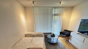 Un dormitorio moderno con cama, una mesita de centro redonda, sofá y televisor.