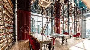 A modern interior with a large table and red chairs, a wine rack, and a view of the city through large windows.