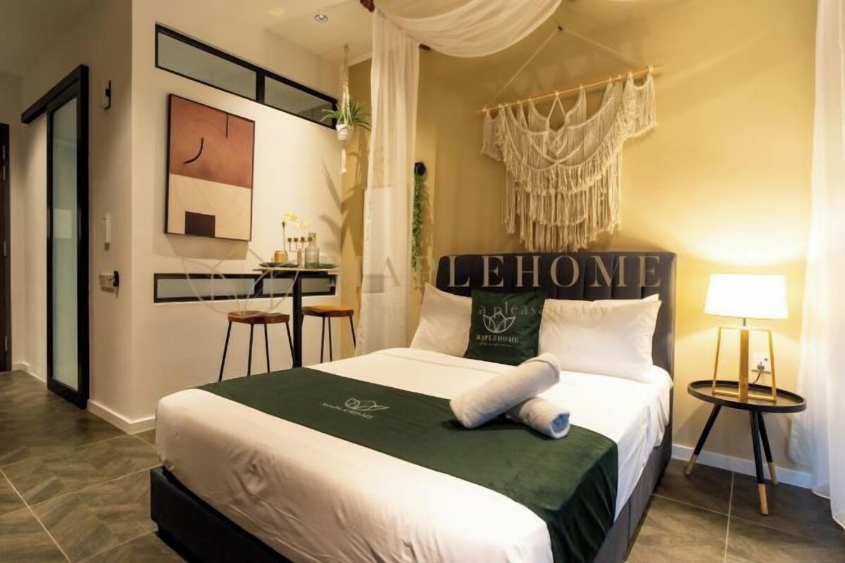 A hotel room with a bed, a desk, a chair, a macrame wall hanging, and a sign that reads "LEHOME".