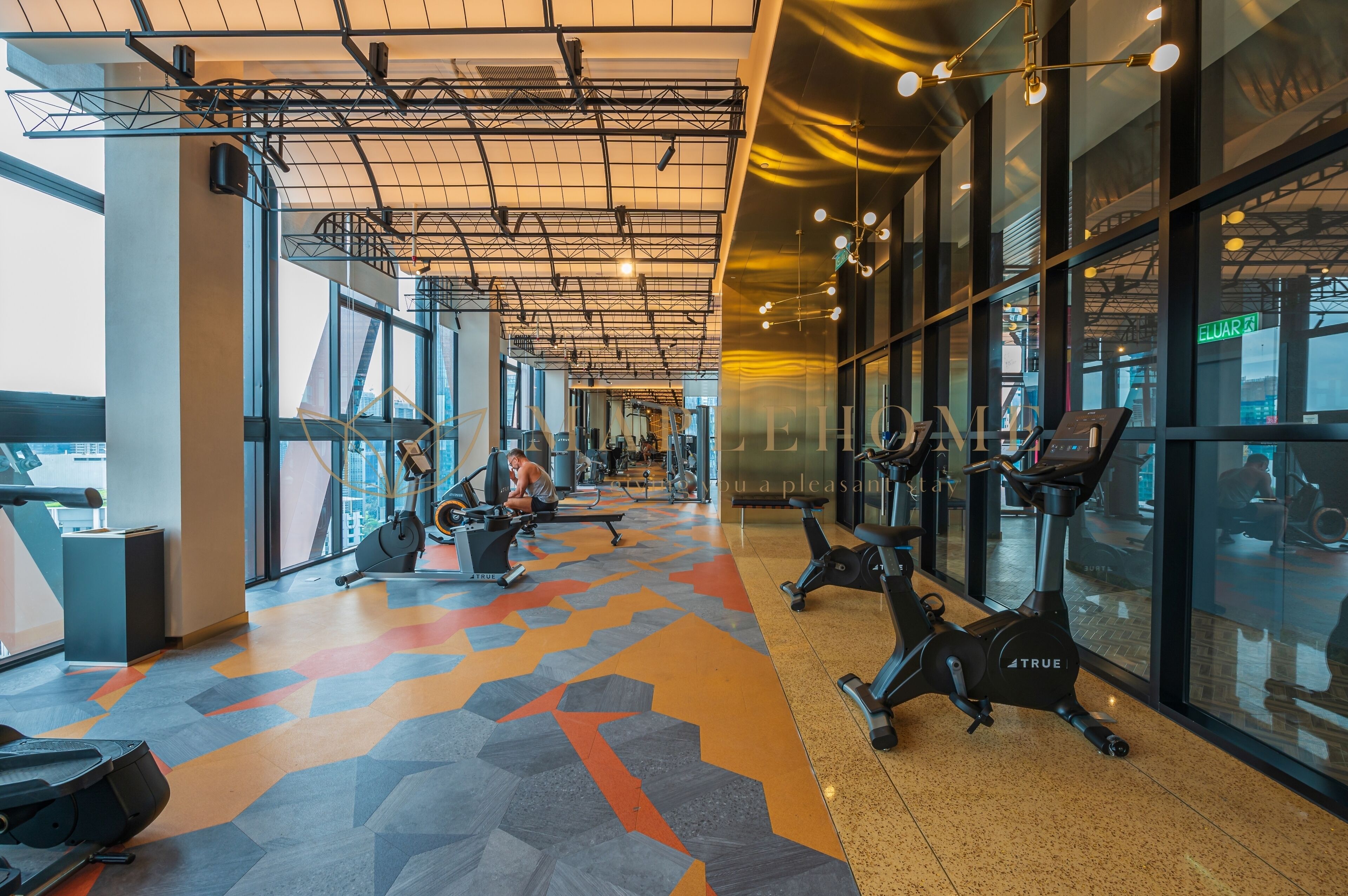 Et fitnesscenter med træningsudstyr, store vinduer og et gulv med geometrisk mønster.