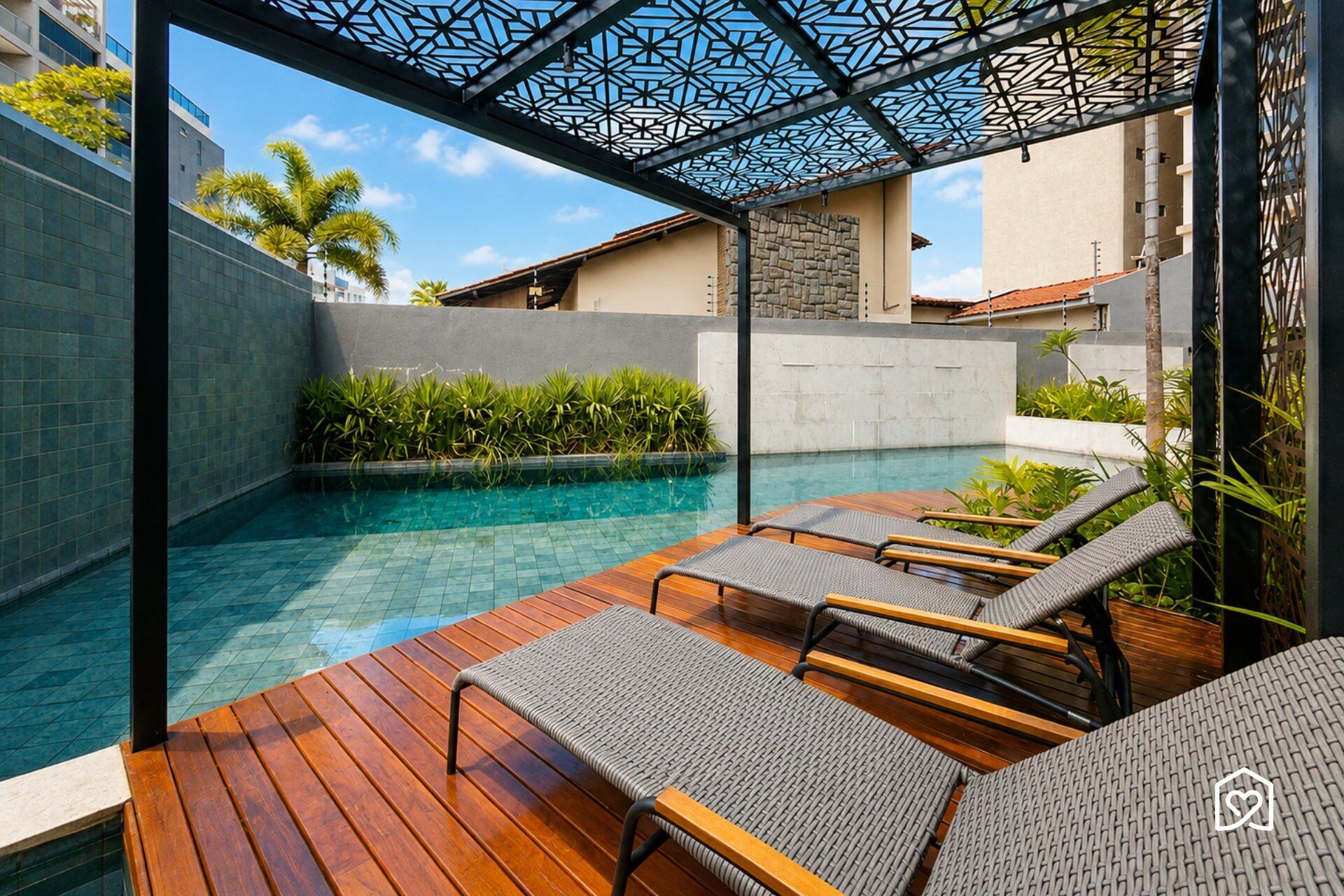 A poolside area with a wooden deck, lounge chairs, and a geometric metal canopy.