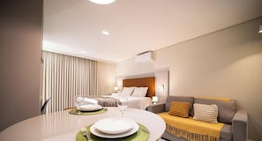 A hotel room with a bed, a sofa, a dining table set with plates and glasses, and a window with curtains.