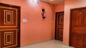 Un pasillo con dos puertas de madera, cada una con una placa numérica, y un detector de incendios en la pared.