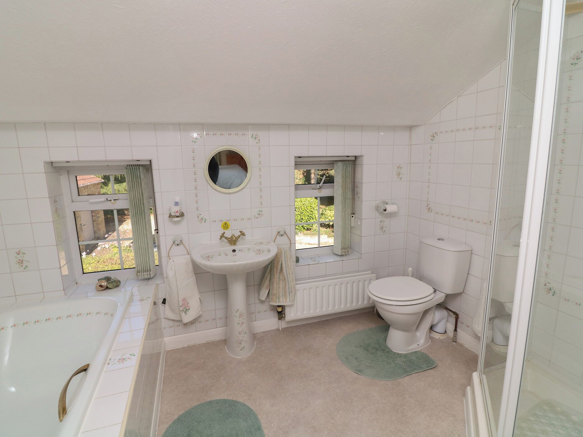 A bathroom with a bathtub, sink, toilet, and two windows with curtains.