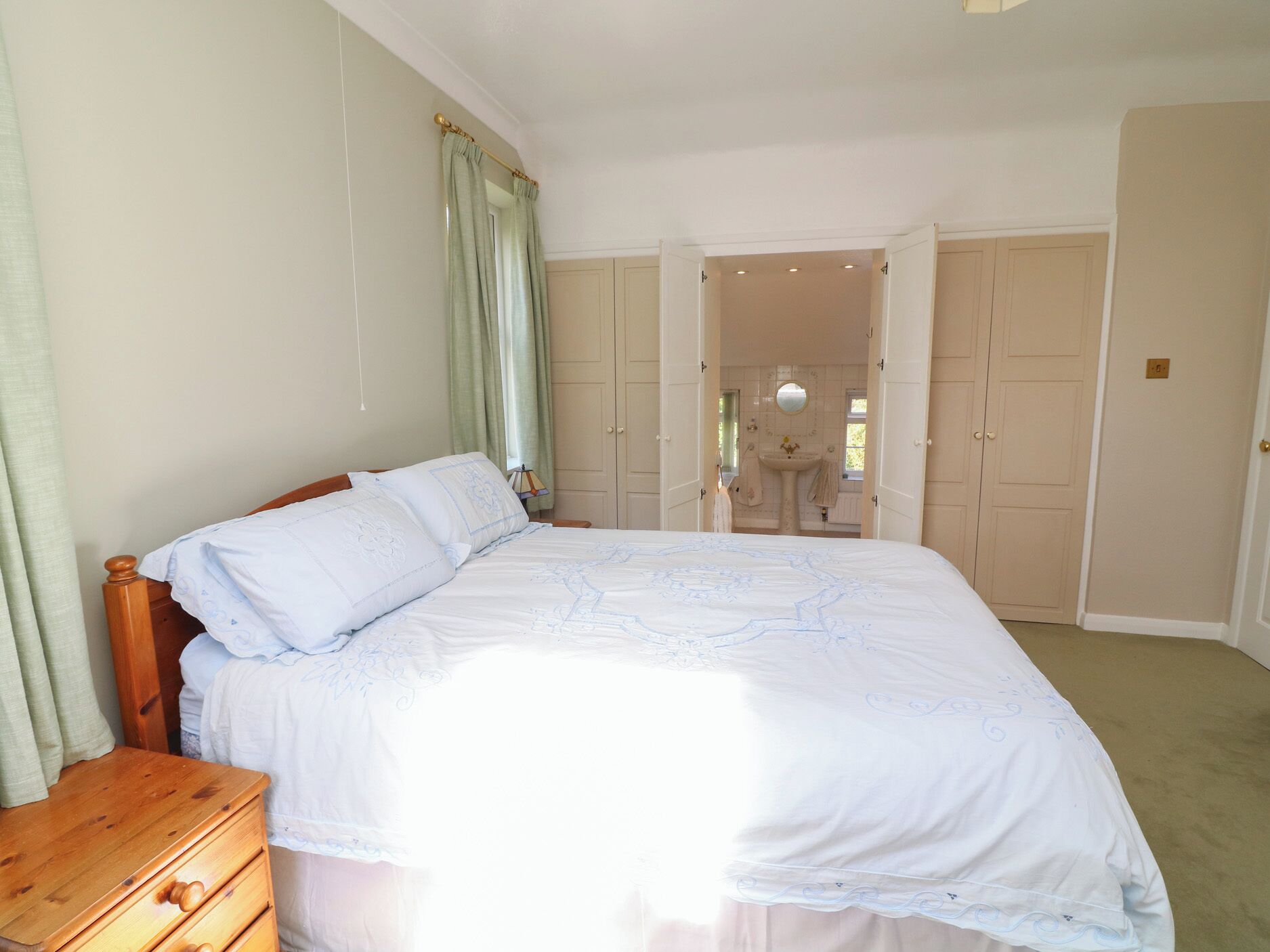Un dormitorio con una cama grande, un aparador de madera y un baño visible a través de una puerta abierta.