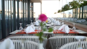 Un salón de restaurante con mesas preparadas para comer, con sillas blancas y manteles individuales rojos.