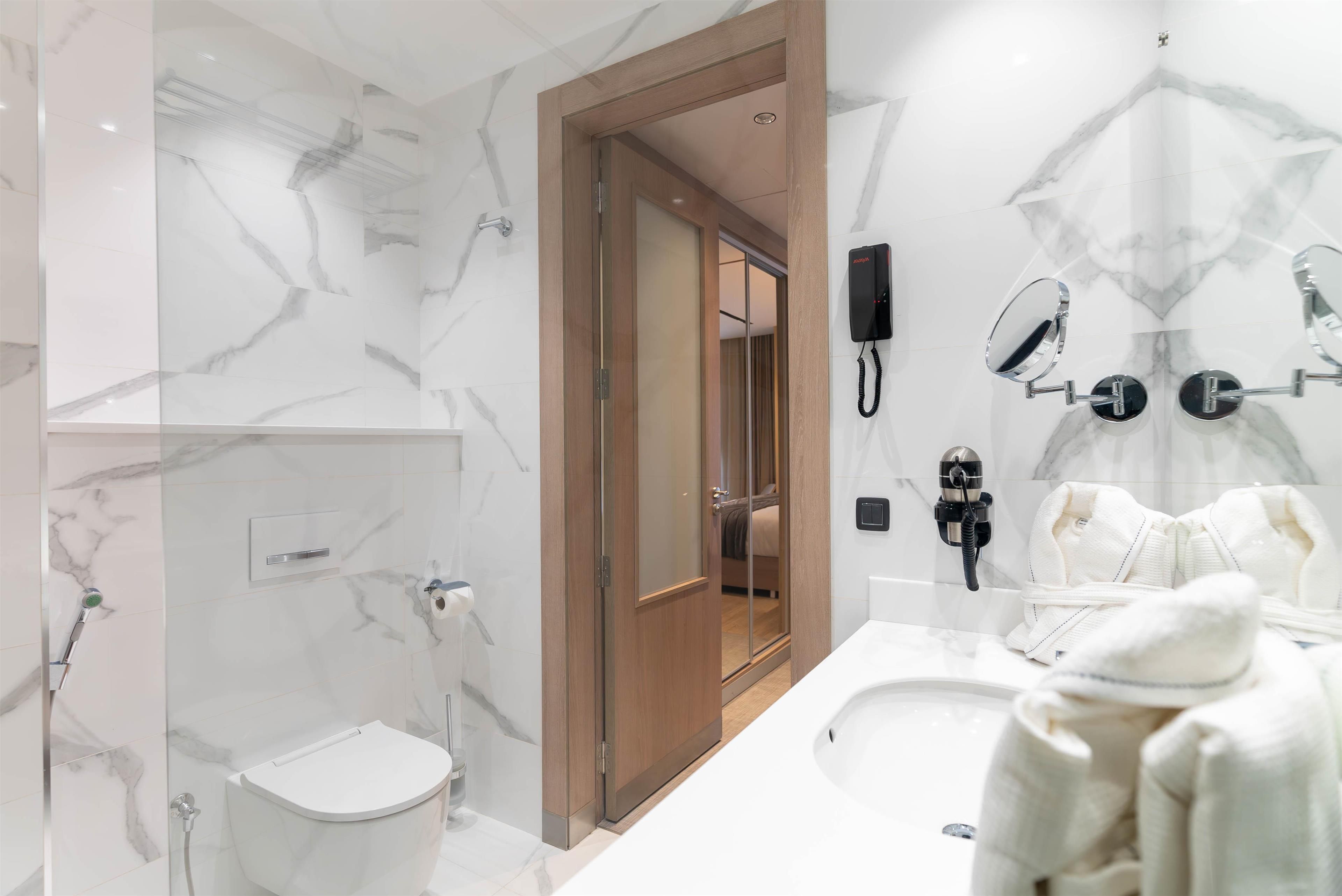 Une salle de bain moderne avec un mur en marbre, une porte en bois, un meuble-lavabo avec un miroir et une douche.