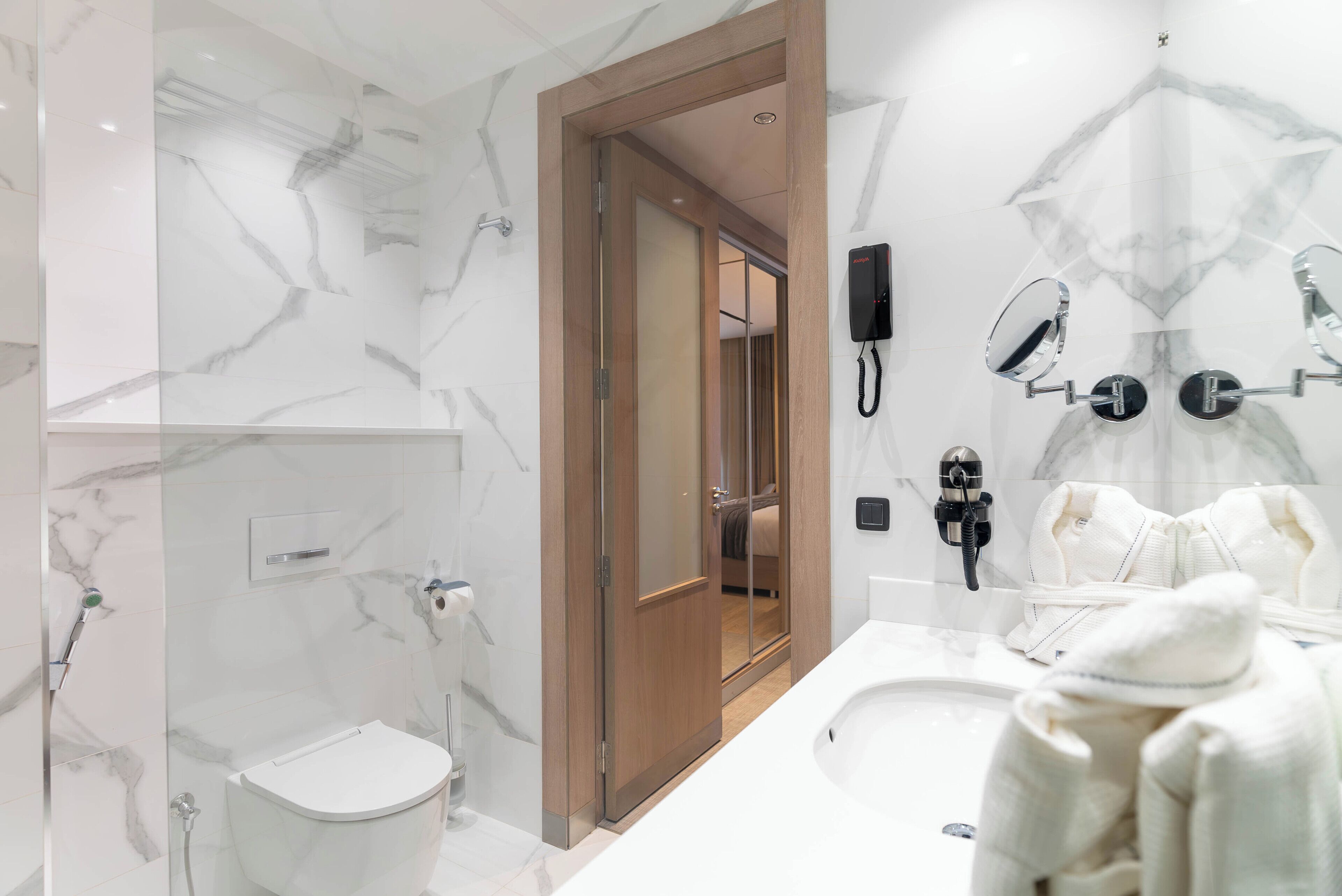 Une salle de bain moderne dotée d’une douche à parois de verre, d’une porte en bois et d’un meuble-lavabo avec un grand miroir et un porte-serviettes.