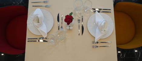 A table set for two with a white tablecloth, silverware, clear glasses, and a red rose centerpiece.