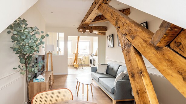 Un espacio habitable estilo loft con vigas de madera a la vista, un sofá, una mesa de comedor y una planta.