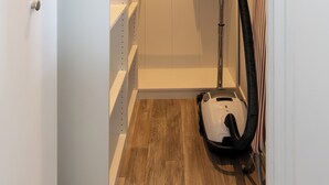 Un vestidor pequeño con suelo de madera, estantes blancos y una aspiradora.