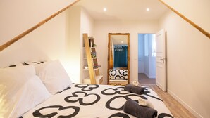 Un dormitorio con cama, almohadas, una mesita de noche, un espejo, un armario y una puerta que da a otra habitación.
