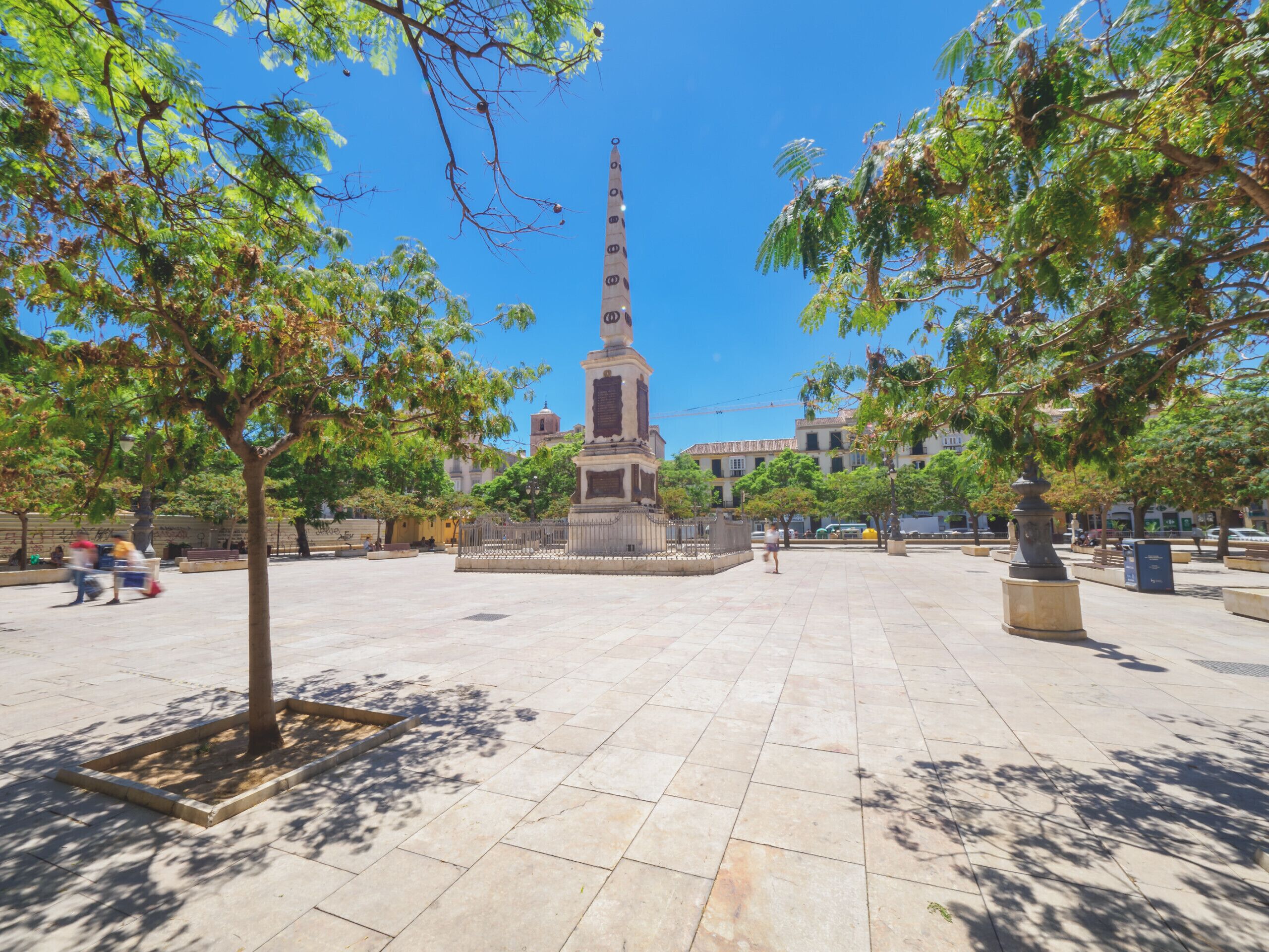 Un'ampia piazza con un monumento centrale, circondata da alberi e edifici sullo sfondo.
