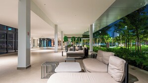 A modern indoor lounge area with a sofa and chairs, a railing, and a view of the outdoors.