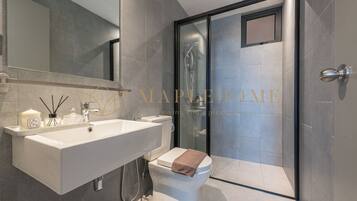 Un baño moderno con un lavamanos grande, inodoro y ducha con mampara de vidrio.