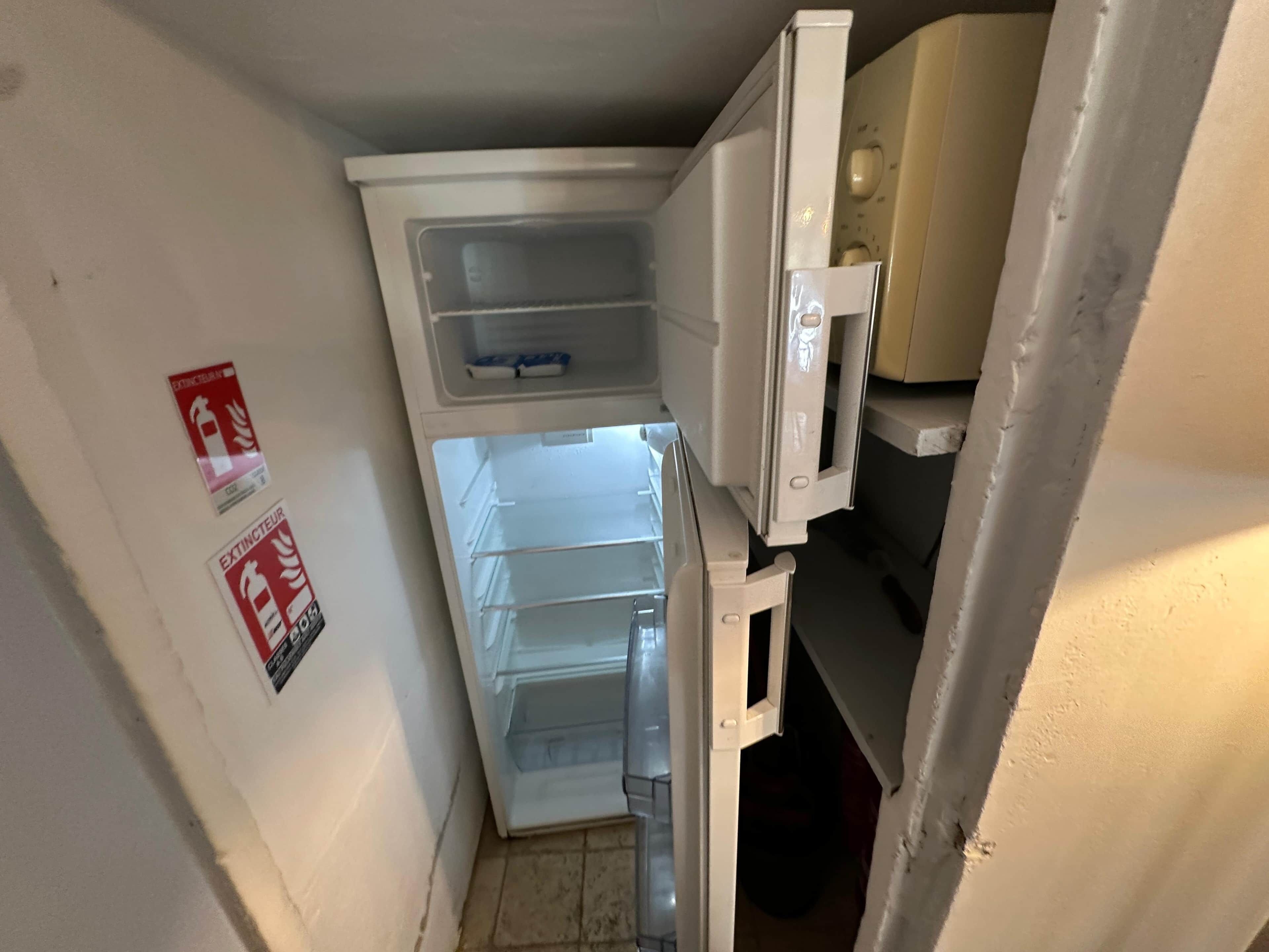 A compact kitchen with a refrigerator, a microwave, and a sink. There are two fire extinguisher signs on the wall.