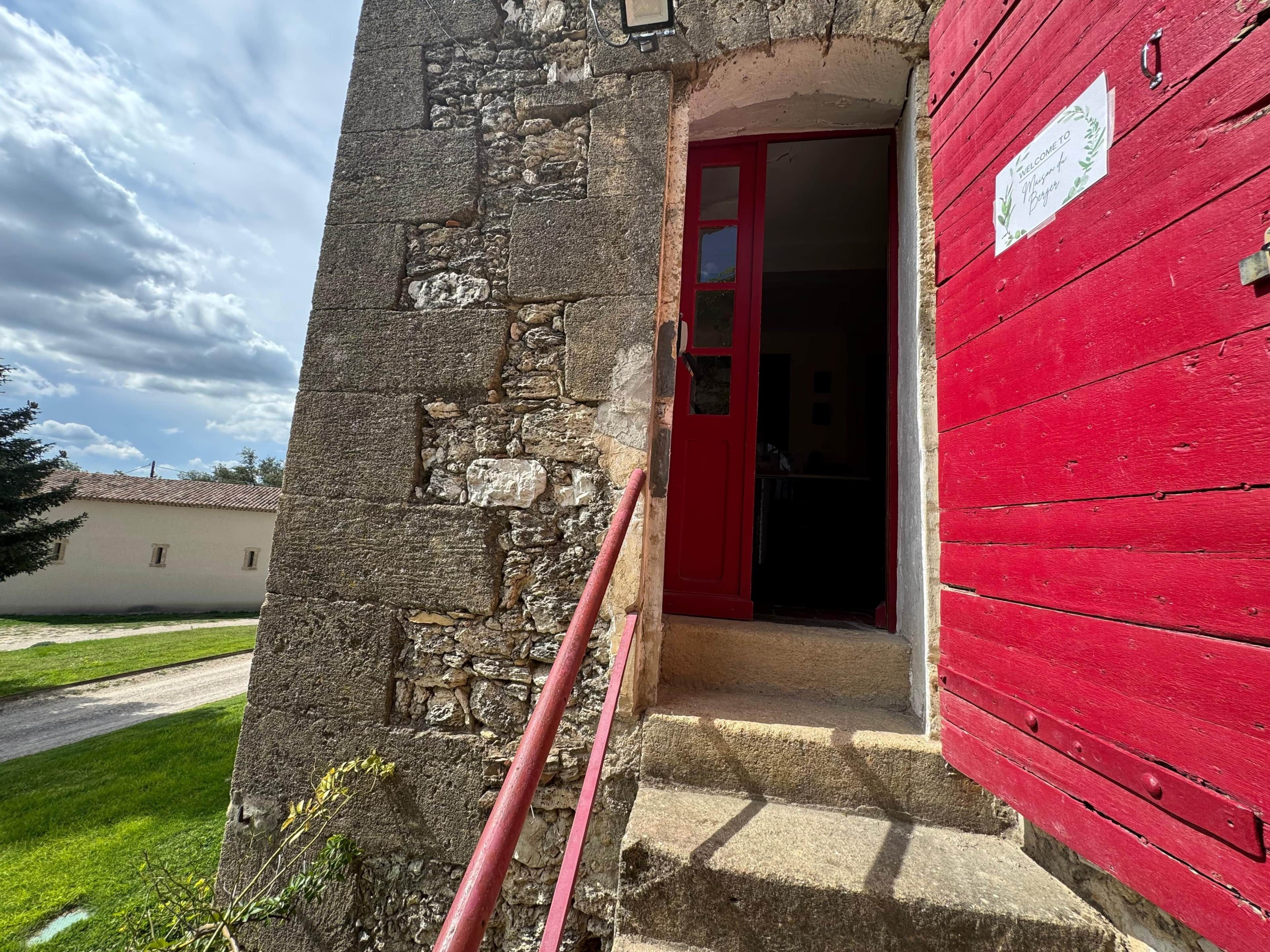 Un bâtiment en pierre avec une porte rouge et une enseigne sur laquelle on peut lire : « Bienvenue chez Burgers ».