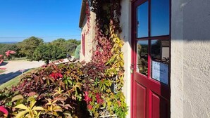 Un bâtiment avec une porte rouge et une pancarte « Bienvenue », entouré d’une végétation luxuriante et sous un ciel bleu dégagé.