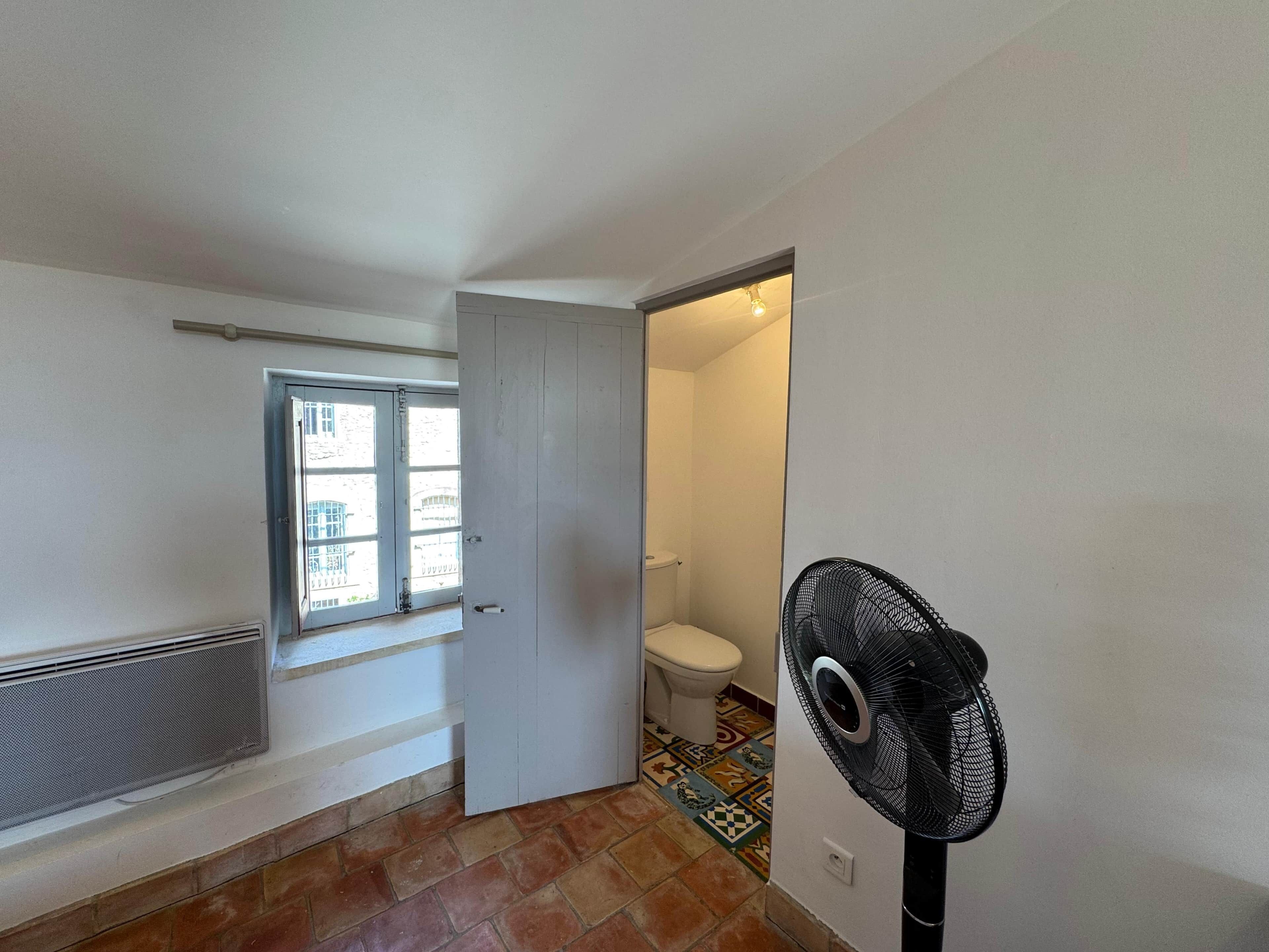 Ein Badezimmer mit Toilette, Fenster und Ventilator.
