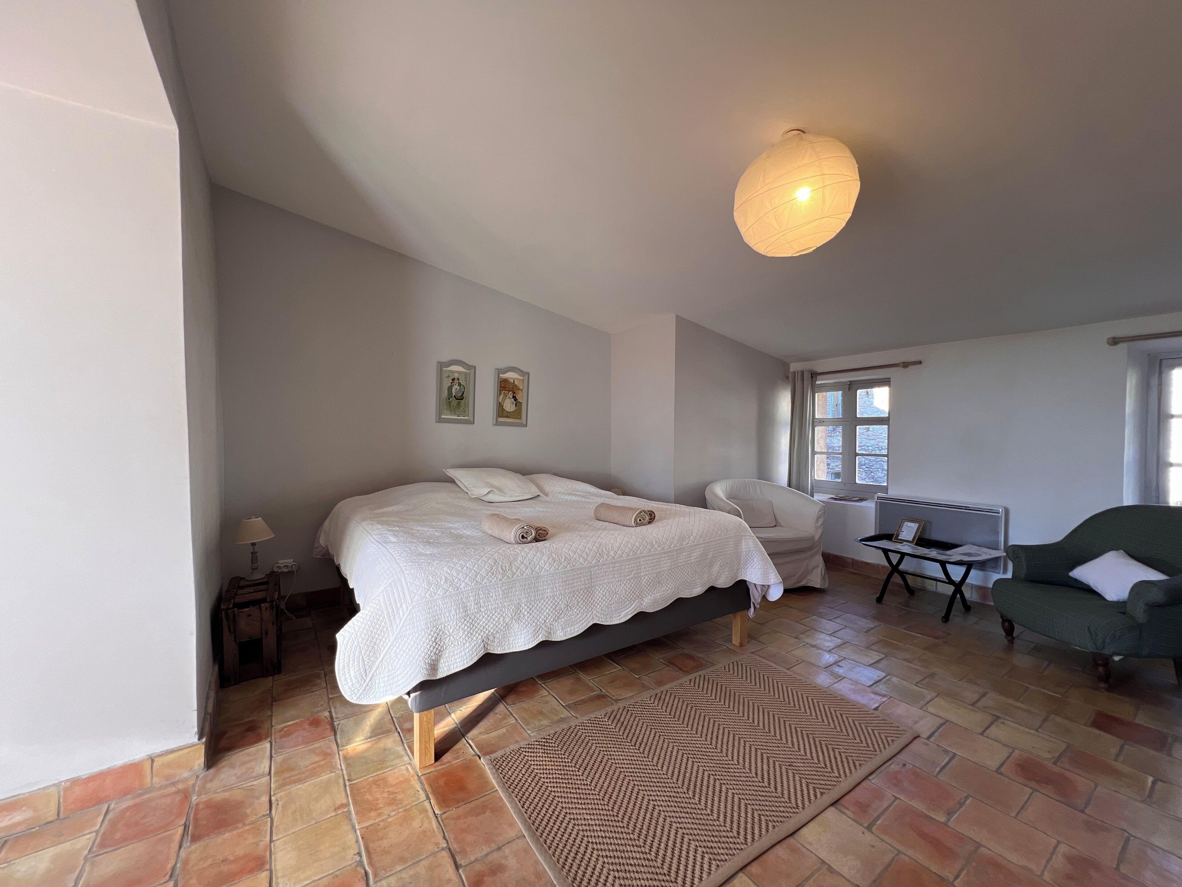 Een slaapkamer met een bed, een stoel, een bureau en een lamp.